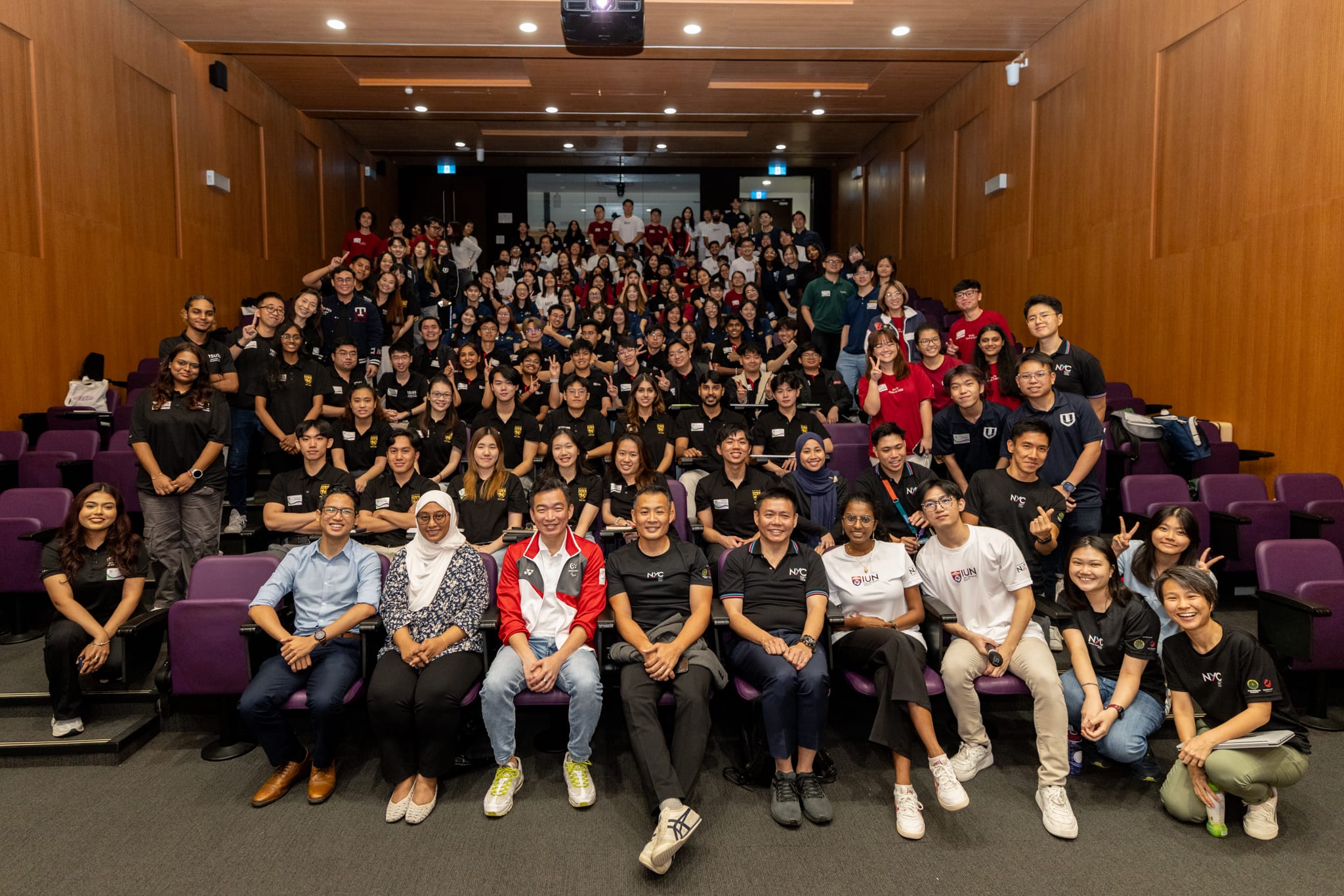 Auditorium with large group of students wearing similar shirts, posing for group photo.